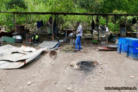 Schweisser 5: Unter diesem Dach arbeiten die Blechner: sie formen aus alten Blechen (z.B. Öltonnen)"neue" Gebrauchsgegenstände: Schüsseln, Öfen, Gartengrill usw. Mit dem Hammer und einem Meissel, manchmal mit einem Zirkel (zwei Metallstäbe mit Schraube) oder einem Muster schneiden sie die Formen und hämmern sie Teile mit Falz zu einer neuen Form. Sie hocken oder sitzen auf einem Stein oder einem Holz, als Unterlage nur ein Stück Stahlträger!